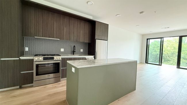 Kitchen with stainless steel range with gas stovetop, modern cabinets, light wood finished floors, tasteful backsplash, and a center island | Image 8