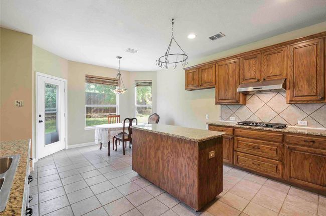 Kitchen with brown cabinets, under cabinet range hood, tasteful backsplash, a center island, and visible vents | Image 14
