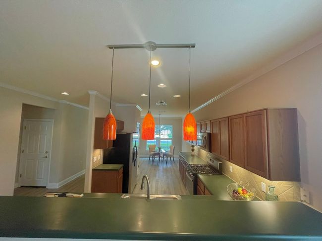 Kitchen with appliances with stainless steel finishes, brown cabinets, ornamental molding, light wood finished floors, and pendant lighting | Image 4