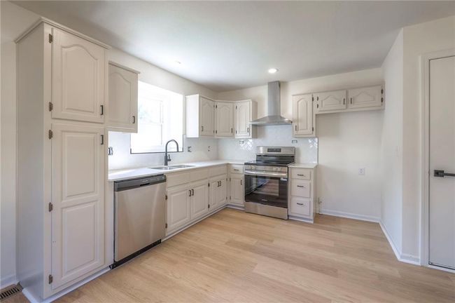 Kitchen featuring appliances with stainless steel finishes, wall chimney exhaust hood, light wood-type flooring, decorative backsplash, and light countertops | Image 7