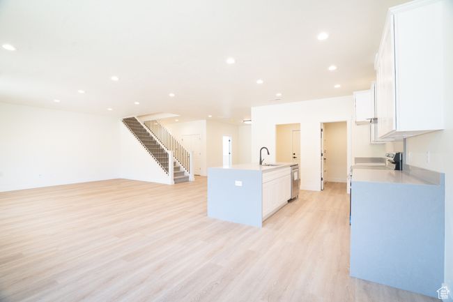 Kitchen with appliances with stainless steel finishes, a kitchen island with sink, white cabinets, light wood-type flooring, and recessed lighting | Image 5