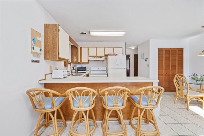 Kitchen with white appliances, under cabinet range hood, light countertops, a peninsula, and light tile patterned flooring | Image 8