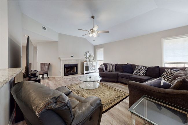 Living area featuring vaulted ceiling, light wood finished floors, ceiling fan, and a fireplace | Image 7
