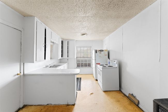 Kitchen with white appliances, a textured ceiling, a peninsula, light countertops, and white cabinetry | Image 9