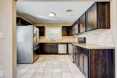 Kitchen featuring dark brown cabinets, sink, light stone countertops, and stainless steel appliances | Image 3