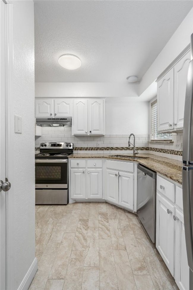 Kitchen with white cabinets, appliances with stainless steel finishes, a sink, decorative backsplash, and under cabinet range hood | Image 8