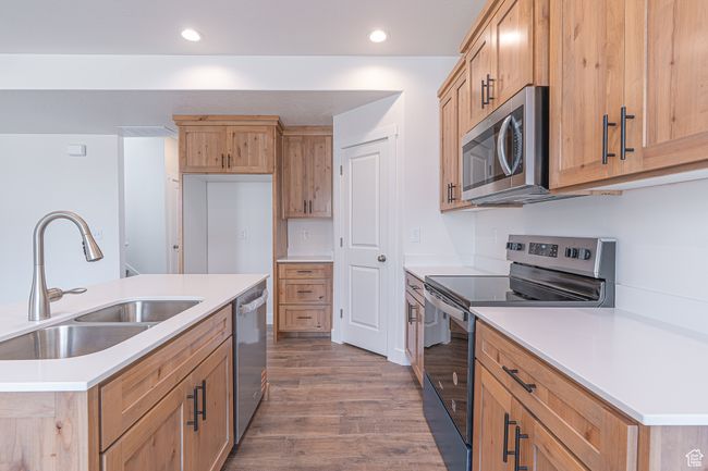 Kitchen with appliances with stainless steel finishes, wood finished floors, recessed lighting, light countertops, and a kitchen island with sink | Image 7