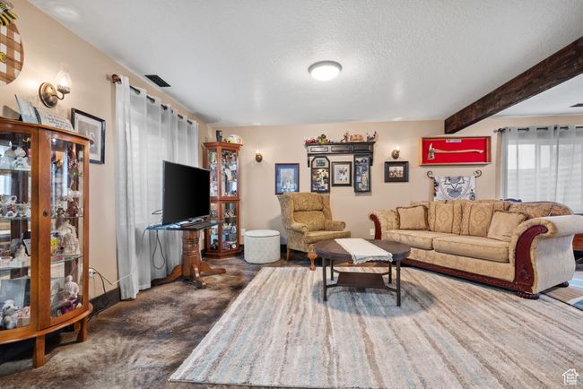 Living area with a textured ceiling, visible vents, beamed ceiling, baseboards, and dark carpet | Image 22