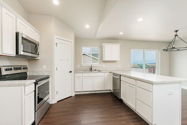 Kitchen with dark wood finished floors, a peninsula, stainless steel appliances, white cabinetry, and a sink | Image 6