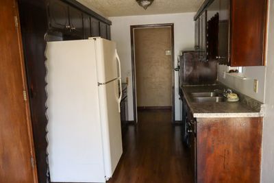 Kitchen with dark wood-type flooring, sink, dark brown cabinetry, white fridge, and a textured ceiling | Image 3