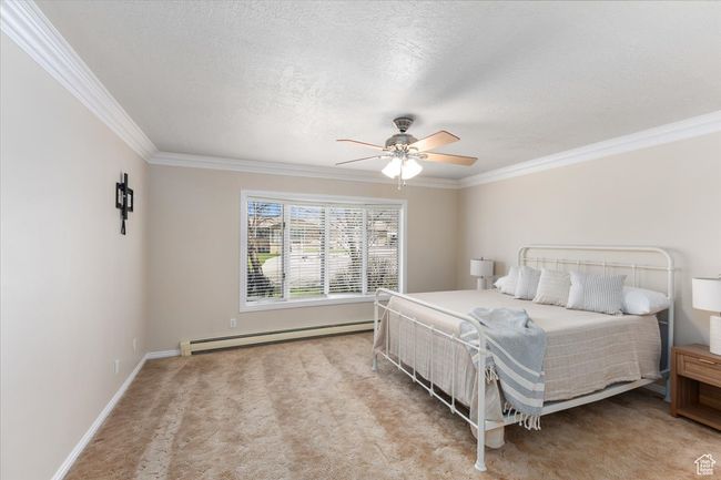 Bedroom with crown molding, a baseboard heating unit, baseboards, and light colored carpet | Image 10