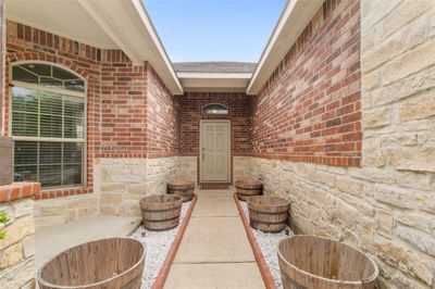 Your new welcoming entryway featuring a brick exterior with stone accents, a covered porch, and a neutral-toned front door. Decorative planters line the pathway, enhancing the home's curb appeal. | Image 2