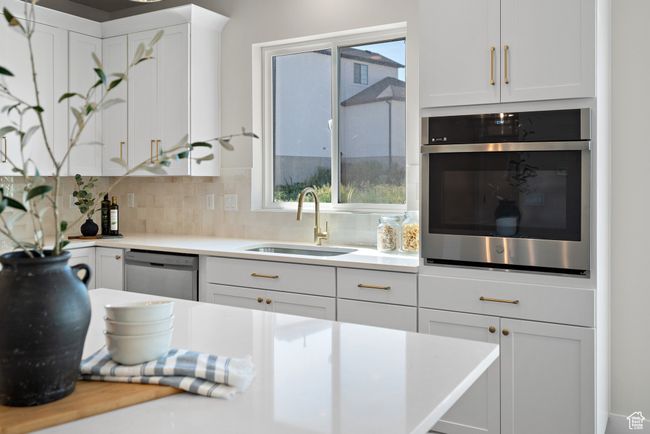 Kitchen with stainless steel appliances, white cabinets, tasteful backsplash, and light countertops | Image 11