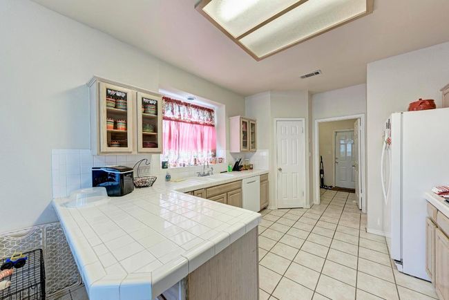 Kitchen featuring white appliances, tile counters, a sink, a peninsula, and decorative backsplash | Image 20