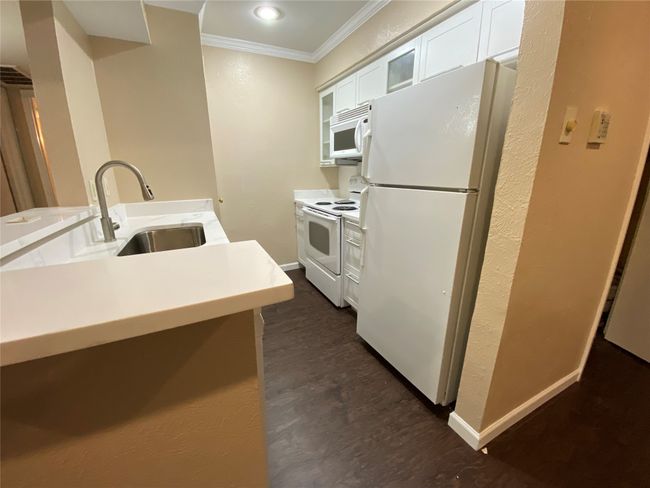 Kitchen with white appliances, light countertops, white cabinets, ornamental molding, and a sink | Image 8