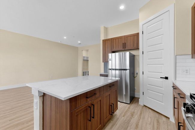 Kitchen with freestanding refrigerator, light wood-style floors, a kitchen island, light stone countertops, and recessed lighting | Image 16