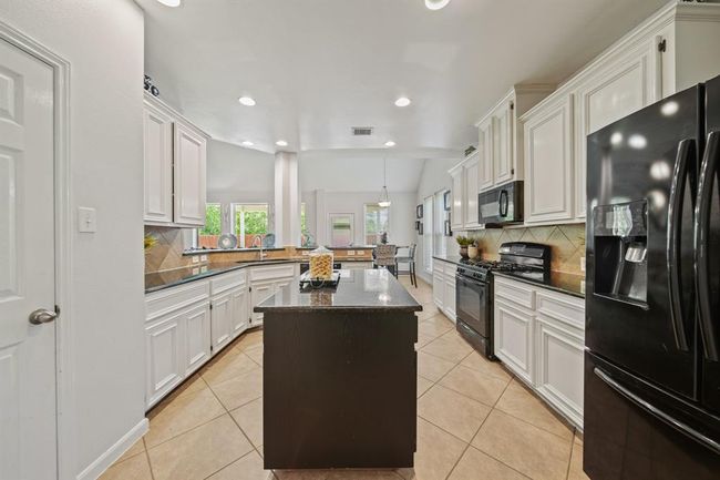 A dark-stained center island adds contrast and extra prep space, while the surrounding layout provides ample storage and workspace for the home chef. | Image 22