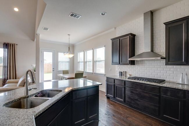 Kitchen featuring wall chimney range hood, dark wood finished floors, a sink, and visible vents | Image 12