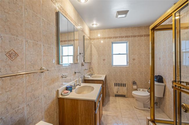 Full bathroom featuring tile patterned floors, toilet, a sink, radiator heating unit, and tile walls | Image 8