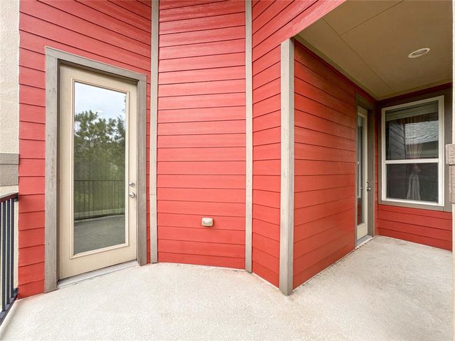 This photo showcases a vibrant red exterior with modern wood siding and two glass doors leading to a balcony or patio. The space is covered, providing shelter and a cozy outdoor area. | Image 24