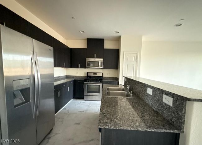 Kitchen with marble finish floor, appliances with stainless steel finishes, a kitchen island with sink, a sink, and dark cabinetry | Image 5