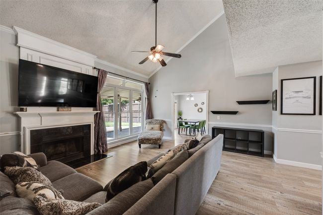 Living room featuring a textured ceiling, a ceiling fan, high vaulted ceiling, wood finished floors, and a high end fireplace | Image 7