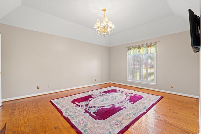 Empty room featuring wood finished floors, a chandelier, and vaulted ceiling | Image 11