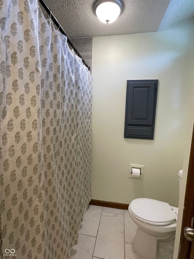bathroom with a textured ceiling, marble look tile flooring, and curtained shower | Image 5