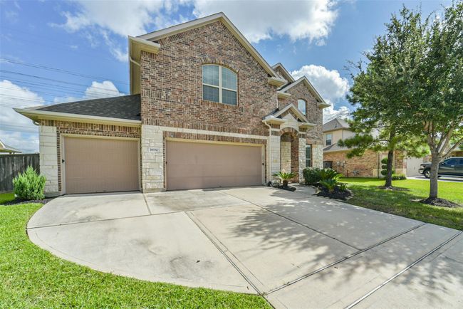 This photo showcases a two-story brick house with a spacious three-car garage. The exterior features a well-maintained lawn and mature trees, providing a welcoming curb appeal. The driveway offers ample parking space, and the home is situated in a suburban neighborhood under a clear blue sky. | Image 31