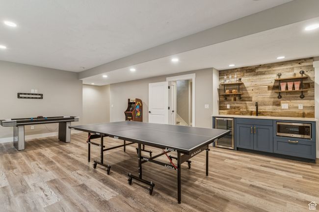 Rec room featuring wine cooler, bar with sink, light wood finished floors, recessed lighting, and wood walls | Image 55