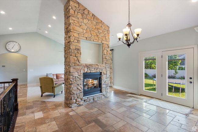 Living room with stone tile flooring, a chandelier, a stone fireplace, baseboards, and recessed lighting | Image 6