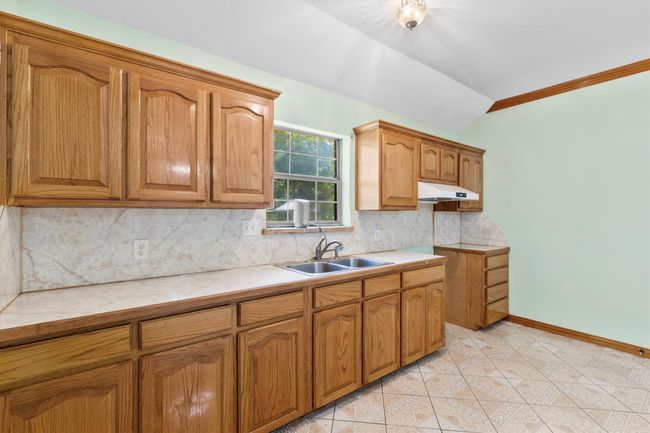 Kitchen featuring a sink, lofted ceiling, light countertops, decorative backsplash, and brown cabinetry | Image 20