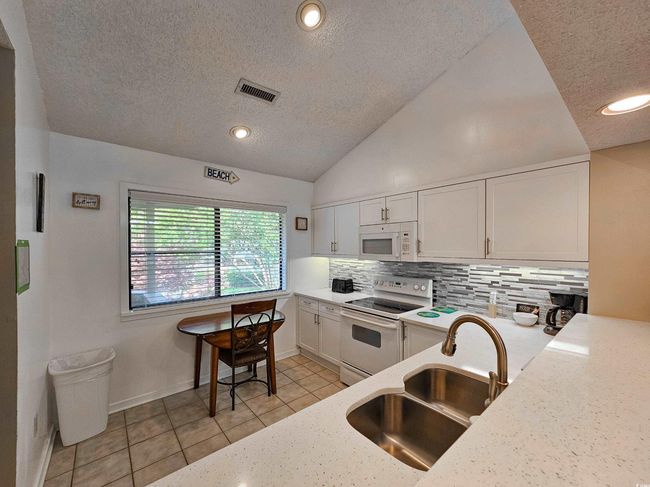 Kitchen with white appliances, a sink, a textured ceiling, tasteful backsplash, and light tile patterned floors | Image 11
