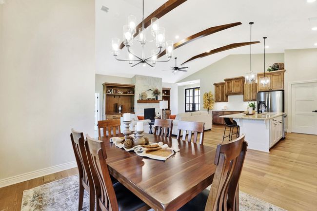 Dining room featuring ceiling fan with notable chandelier, high vaulted ceiling, light hardwood / wood-style flooring, and a fireplace | Image 17