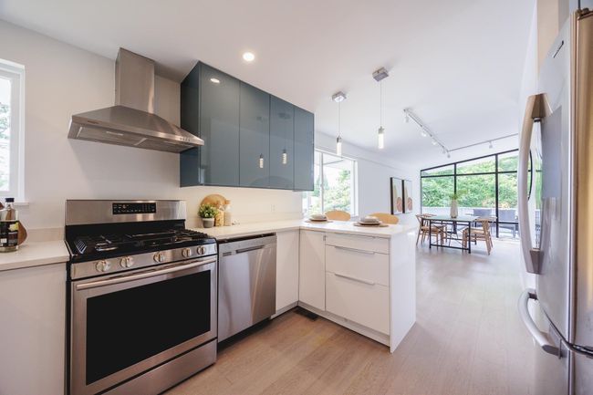 Kitchen featuring wall chimney exhaust hood, appliances with stainless steel finishes, a peninsula, light wood-style floors, and light countertops | Image 4