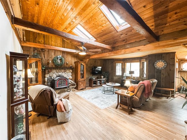 Living area featuring lofted ceiling with skylight, wood walls, and wood finished floors | Image 5
