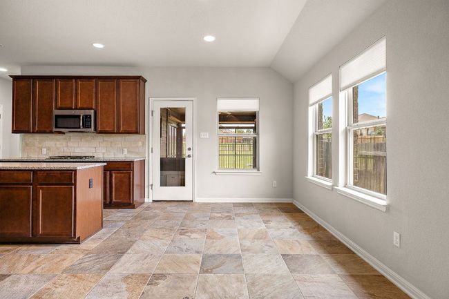 Kitchen featuring vaulted ceiling, stone finish flooring, decorative backsplash, stainless steel microwave, and baseboards | Image 9