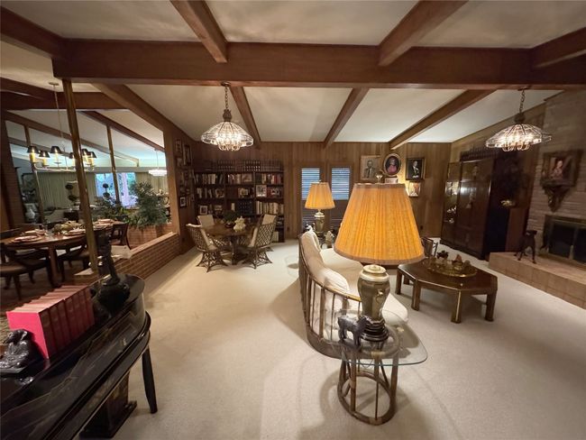 Living room featuring a chandelier, beam ceiling, wooden walls, a fireplace, and light colored carpet | Image 17