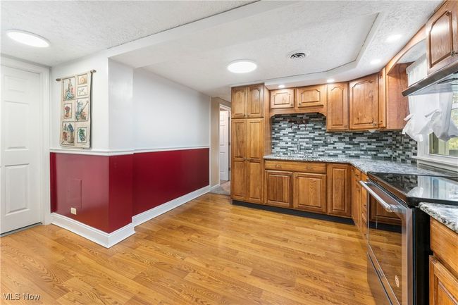 Kitchen featuring light wood-style flooring, stainless steel range with electric cooktop, brown cabinetry, backsplash, and a textured ceiling | Image 16