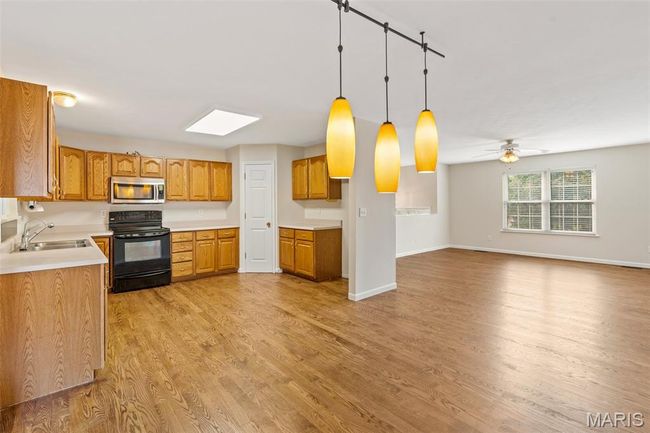 Kitchen with black electric range oven, a sink, stainless steel microwave, light wood-style flooring, and brown cabinetry | Image 12