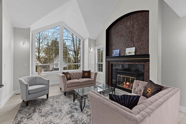 Living room with a fireplace, baseboards, wood finished floors, and lofted ceiling | Image 4