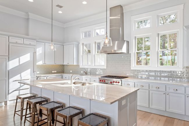 Kitchen featuring light wood finished floors, ornamental molding, a sink, a breakfast bar area, and wall chimney range hood | Image 10
