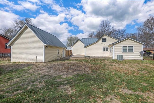 View of property exterior with fence, metal roof, central AC unit, a patio area, and a lawn | Image 11