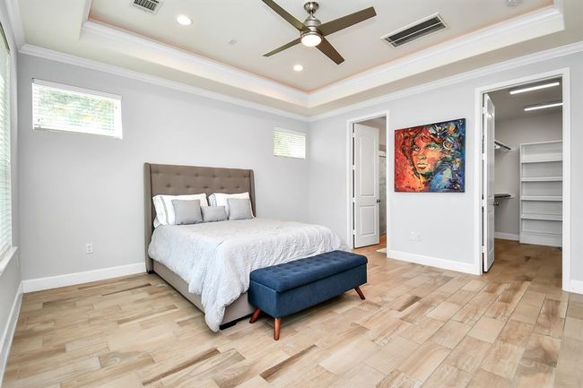 Bright and spacious bedroom with a modern ceiling fan and elegant wood flooring. Features a cozy bed, vibrant wall art, and a walk-in closet, offering a comfortable and stylish living space. | Image 14