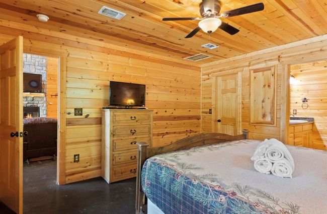 Bedroom with wood ceiling, wood walls, a fireplace, ensuite bathroom, and finished concrete flooring | Image 15