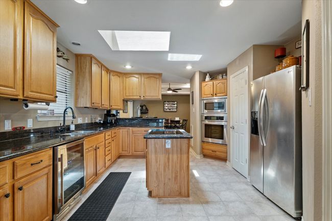 Kitchen with appliances with stainless steel finishes, a sink, beverage cooler, a skylight, and a kitchen island | Image 16
