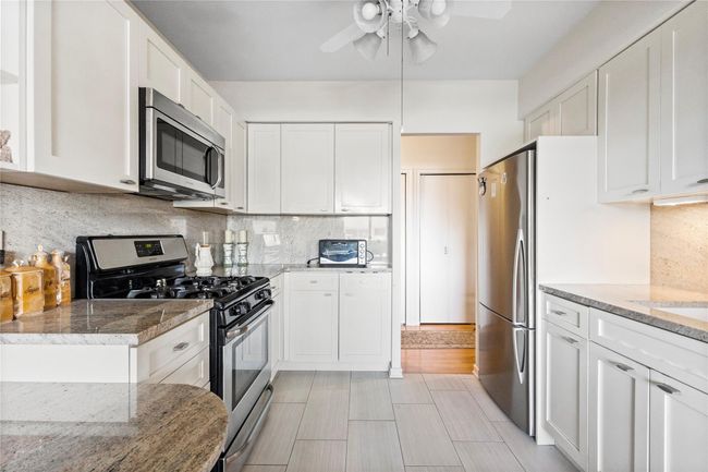 Kitchen featuring stainless steel appliances, ceiling fan, white cabinetry, backsplash, and light stone counters | Image 8