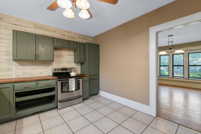 Kitchen with green cabinets, electric range, butcher block counters, light tile patterned floors, and ceiling fan | Image 12