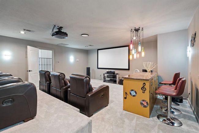 Stylish media room on the second floor, featuring an eclectic light fixture over the bar and elevated seating. A projector and screen create the ultimate home theater experience. | Image 30