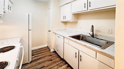 Modern kitchen boasting sleek white cabinetry, marble-like countertops, and wood-style vinyl plank flooring; complete with essential appliances and recent pex pipes!. | Image 3